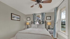 A bedroom with a bed, two bedside tables with lamps, a ceiling fan, and a window with curtains.