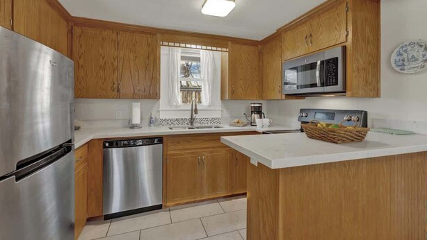 A modern kitchen with wooden cabinets, stainless steel appliances, and a white countertop.