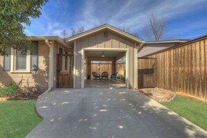 Una casa residencial con un porche cubierto, entrada para vehículos y patio trasero cercado.