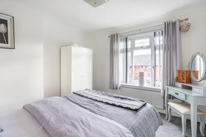 Un dormitorio con cama, cómoda, espejo y ventana con cortinas.