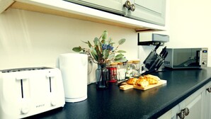 A kitchen counter with a toaster, a microwave, a plant, and a cutting board with bread.