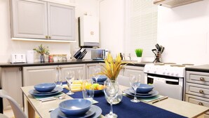 A kitchen with white cabinets, a microwave, a stove, and a dining table set with blue plates and glasses.