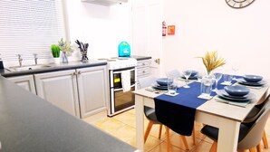 A modern kitchen with white cabinets, a stove, and a sink. There is a dining table with blue tablecloths and plates.