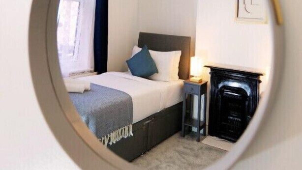 A round mirror reflecting a bedroom with a bed, nightstand, and fireplace.