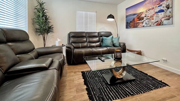 Ein modernes Wohnzimmer mit Ledersofas, einem Glastisch und einem Gemälde mit einer Küstenlandschaft.