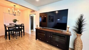 Ein modernes Wohnzimmer mit einem großen Flachbildfernseher, dunklem Holzmöbel und einem Essbereich mit Tisch und Stühlen.