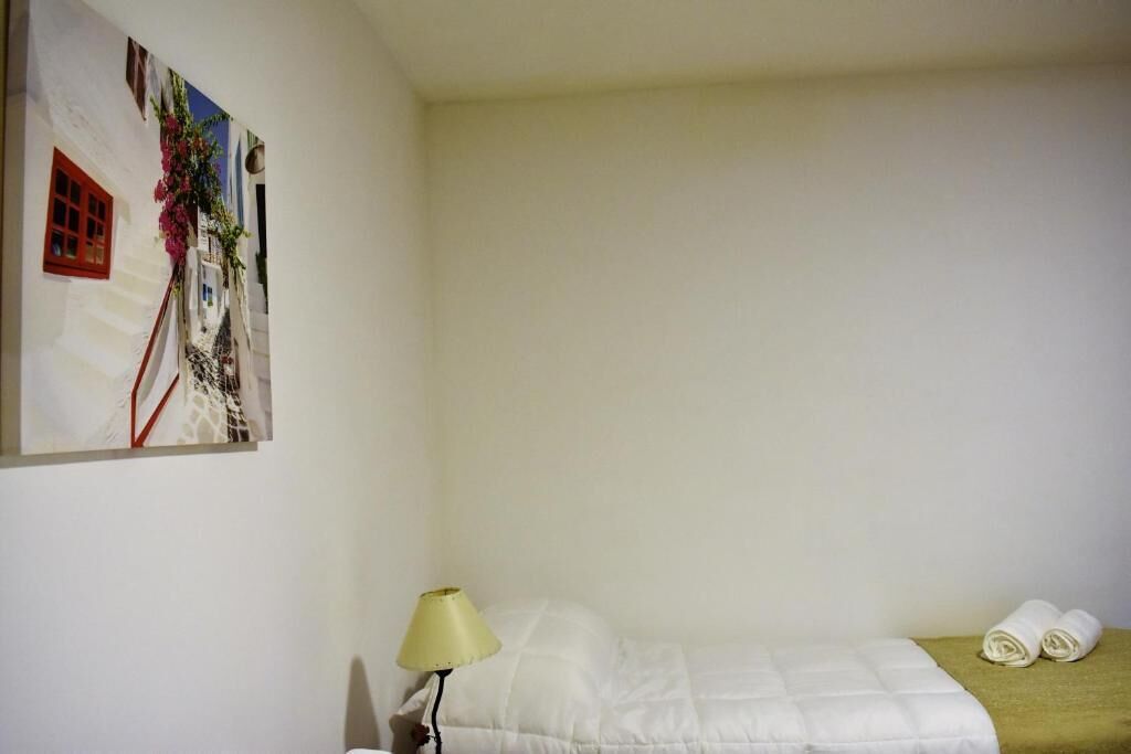 A single bed with a white duvet, a bedside lamp, and a rolled towel on the floor.