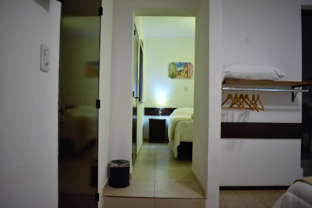 Un couloir étroit mène à une chambre à coucher qui contient un lit, une table de chevet et un portant à vêtements.