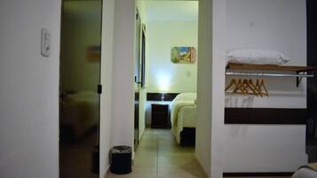 Un couloir étroit mène à une chambre à coucher qui contient un lit, une table de chevet et un portant à vêtements.