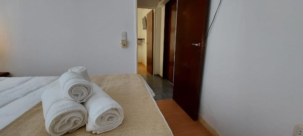 Een hotelkamer met een bed, twee opgerolde handdoeken, een houten deur en een wandlamp.