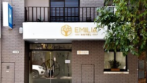 The exterior of Emilia Hotel with a glass entrance, a visible car inside, and a small window with a plant. - EMILIA HOTEL (Rosario)