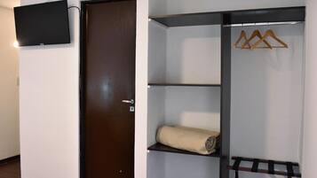 A room with a dark wooden door, a mounted flat-screen TV, and a built-in wardrobe with shelves and a hanging rod.