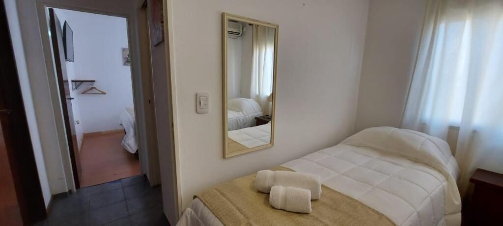 A hotel room with a bed, a mirror, and a door leading to another room.