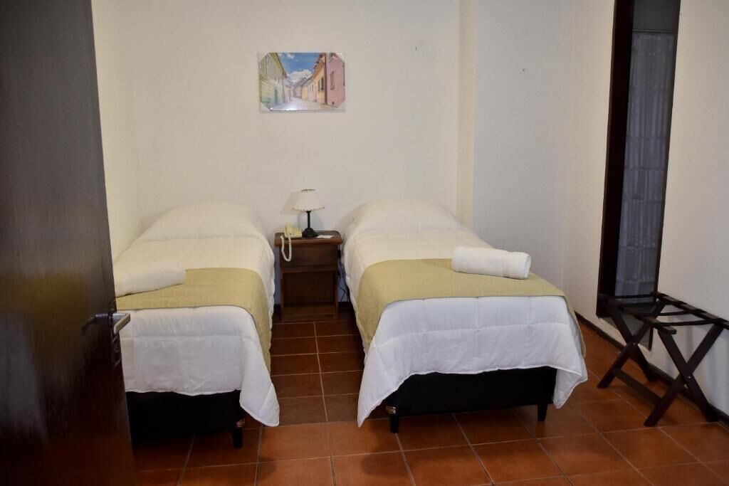 A small room with two beds, a nightstand, a lamp, and a painting on the wall.