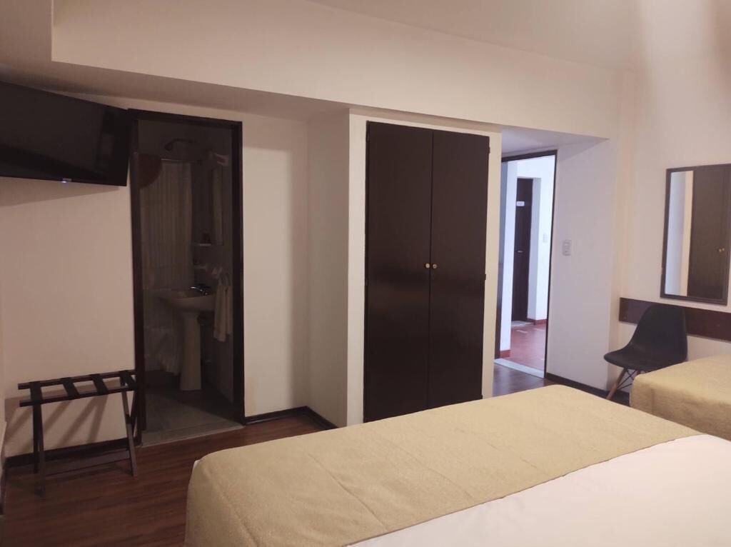 Habitación de hotel con cama, armario, espejo y baño visible a través de una puerta abierta.