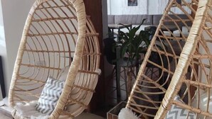 Two wicker hanging chairs with cushions, a wooden-framed mirror, and a tiled floor. - EMILIA HOTEL (Rosario)