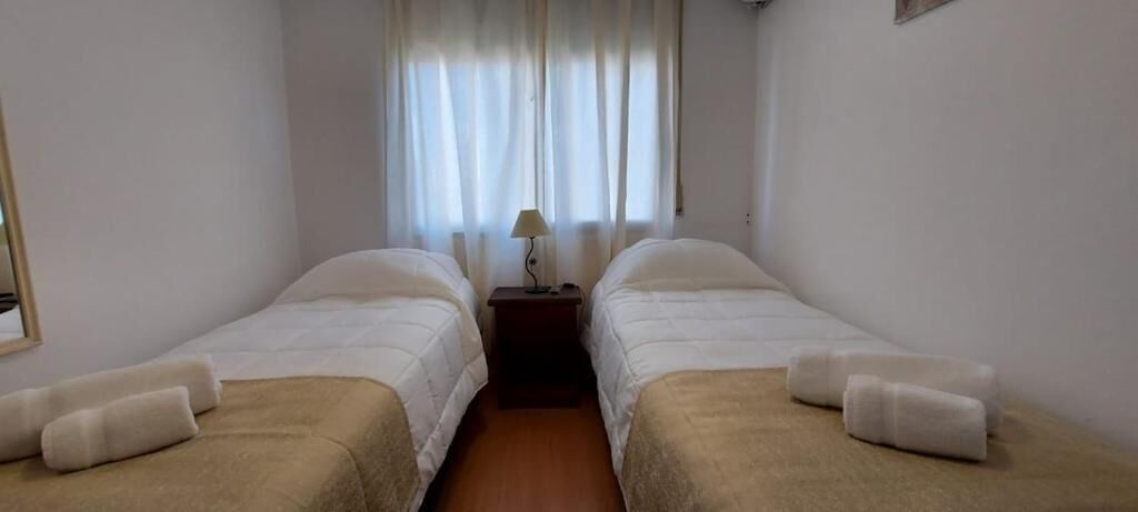 A room with two single beds, a nightstand with a lamp, and a window with curtains.
