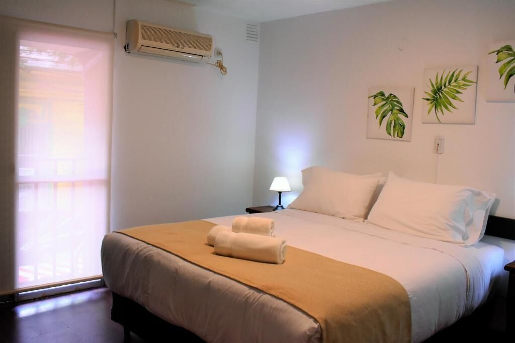 Una habitación de hotel con cama, mesita de noche, lámpara y ventana con persianas.