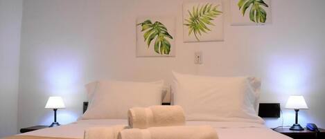Una habitación de hotel con una cama, dos lámparas de noche y tres cuadros con motivos vegetales en la pared.