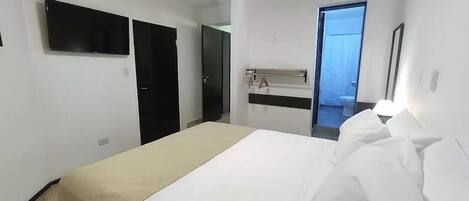 Una habitación de hotel con una cama, un televisor montado en la pared, un espejo y una puerta que da a un balcón.