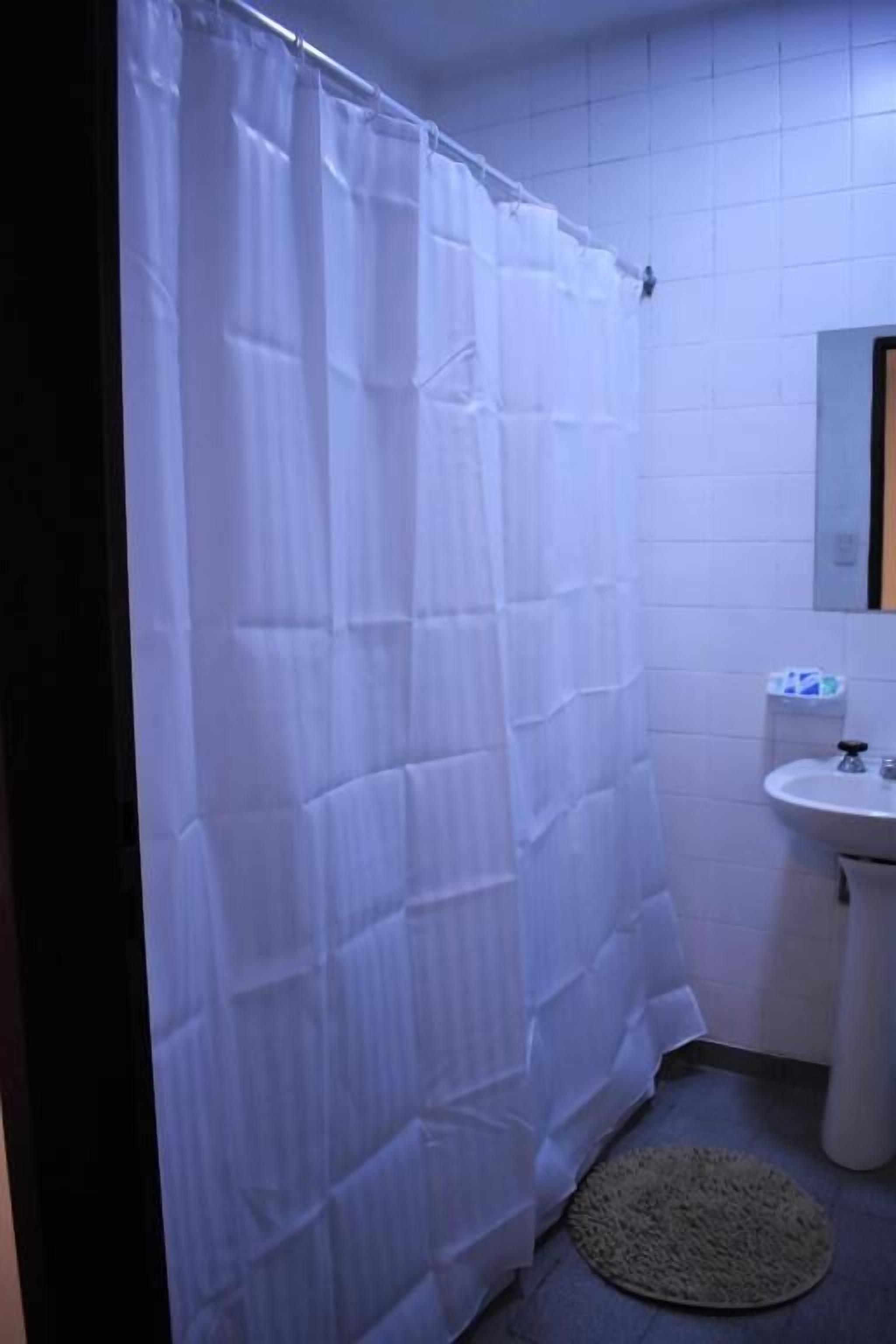 Une salle de bain avec un rideau de douche blanc, un lavabo et un miroir.