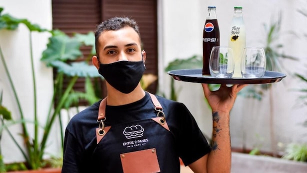 A person holding a tray with two bottles and two glasses. - EMILIA HOTEL (Rosario)