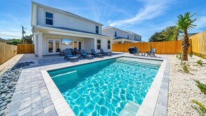 Une maison à deux étages avec une piscine, un espace salon extérieur et une clôture en bois.