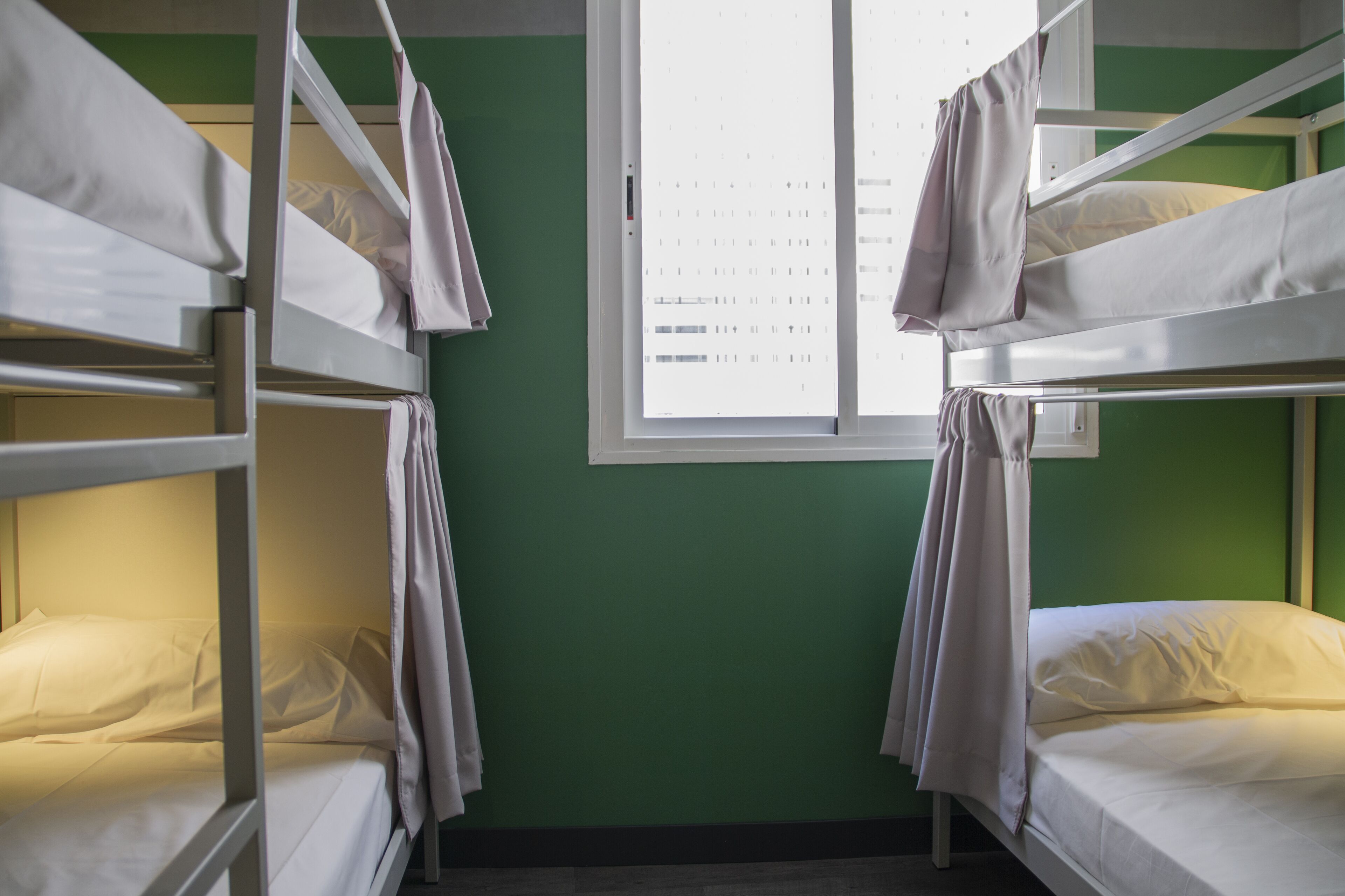 A dormitory room with bunk beds, a window with a view, and a green wall.
