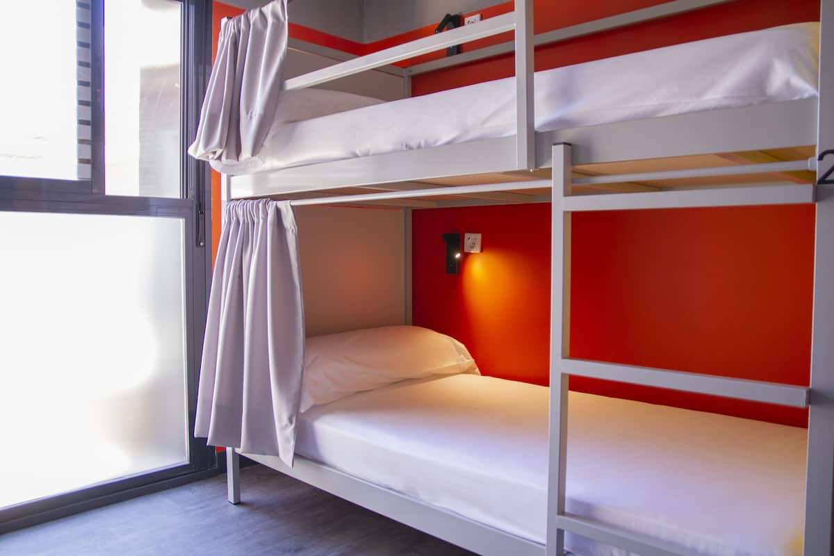 Uma cama beliche com roupa de cama branca e uma parede vermelha.