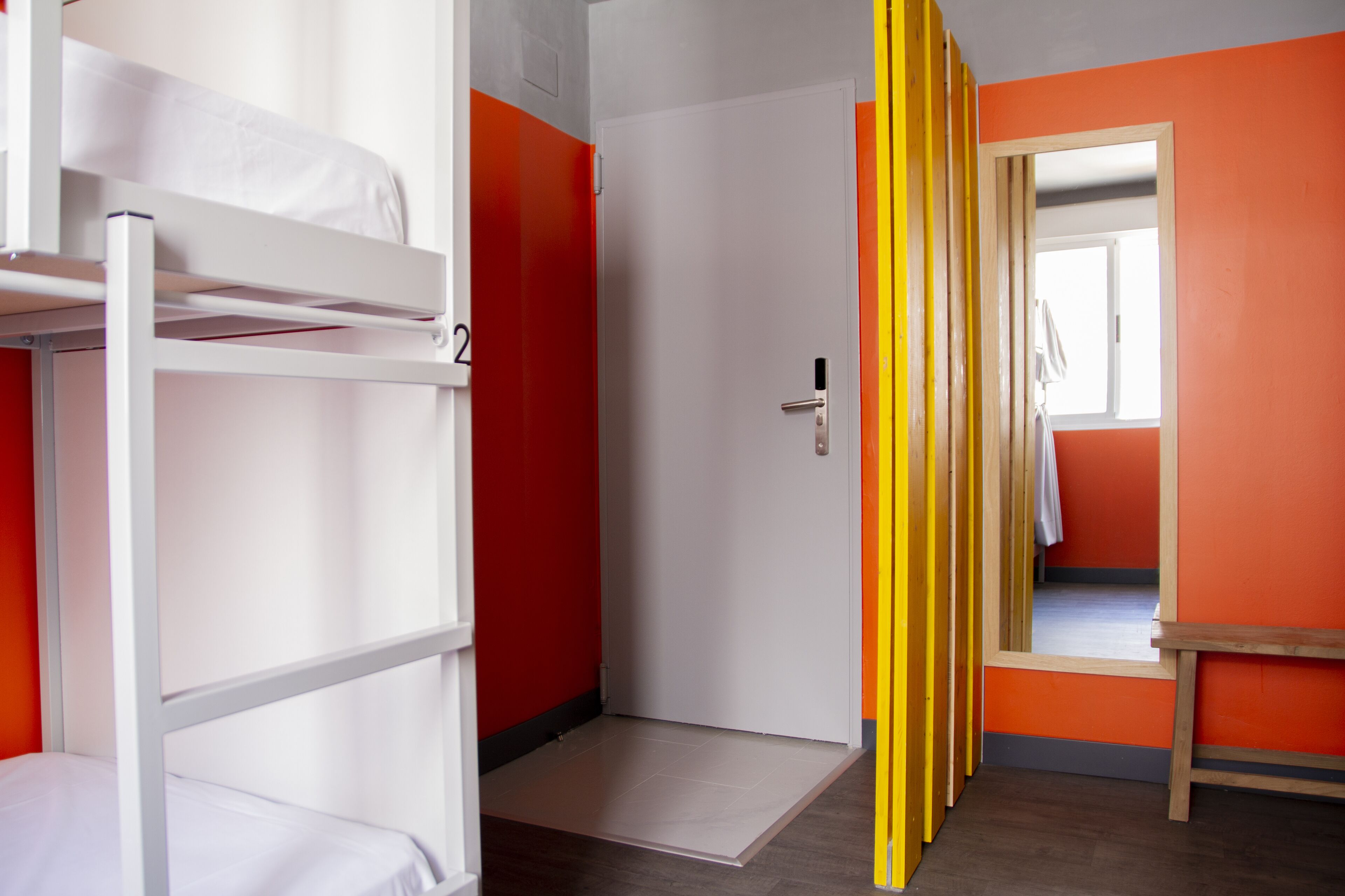 A dormitory room with bunk beds, a door, and a bright orange wall.