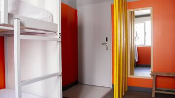 Una habitació de dormitori amb llits superposats, una porta i una paret de color taronja brillant.