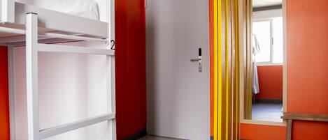 A dormitory room with bunk beds, a door, and a bright orange wall.