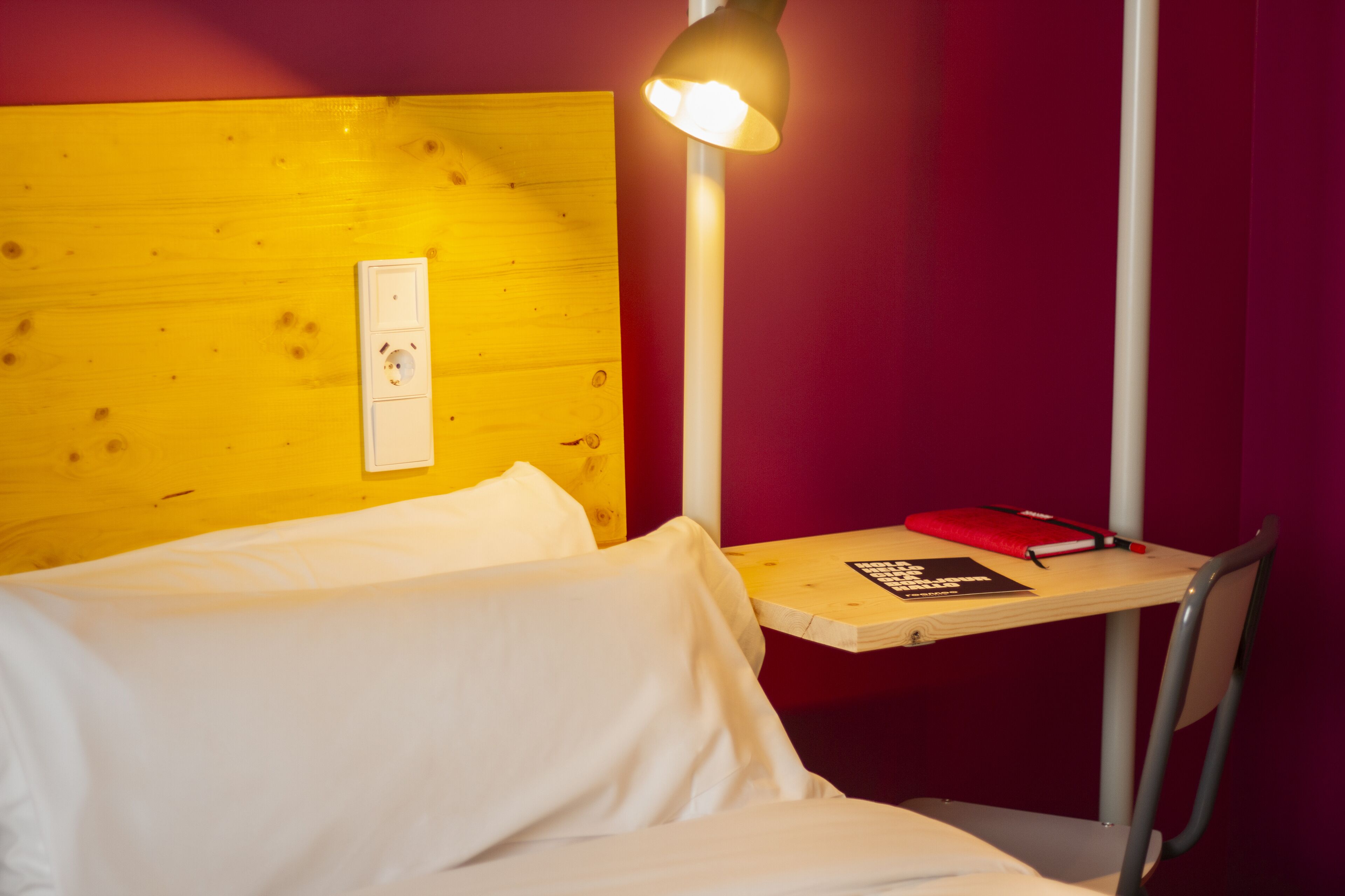 Una habitación con cama, un escritorio con lámpara y una silla.