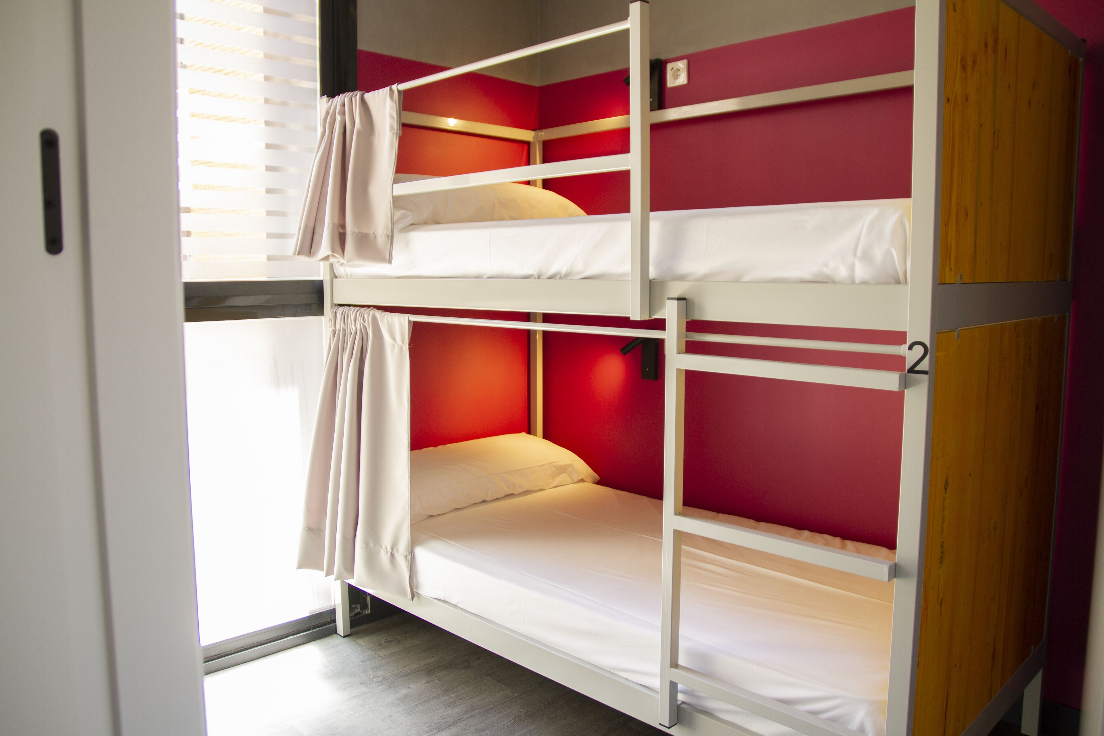 A bunk bed room with a window, red walls, and a door.