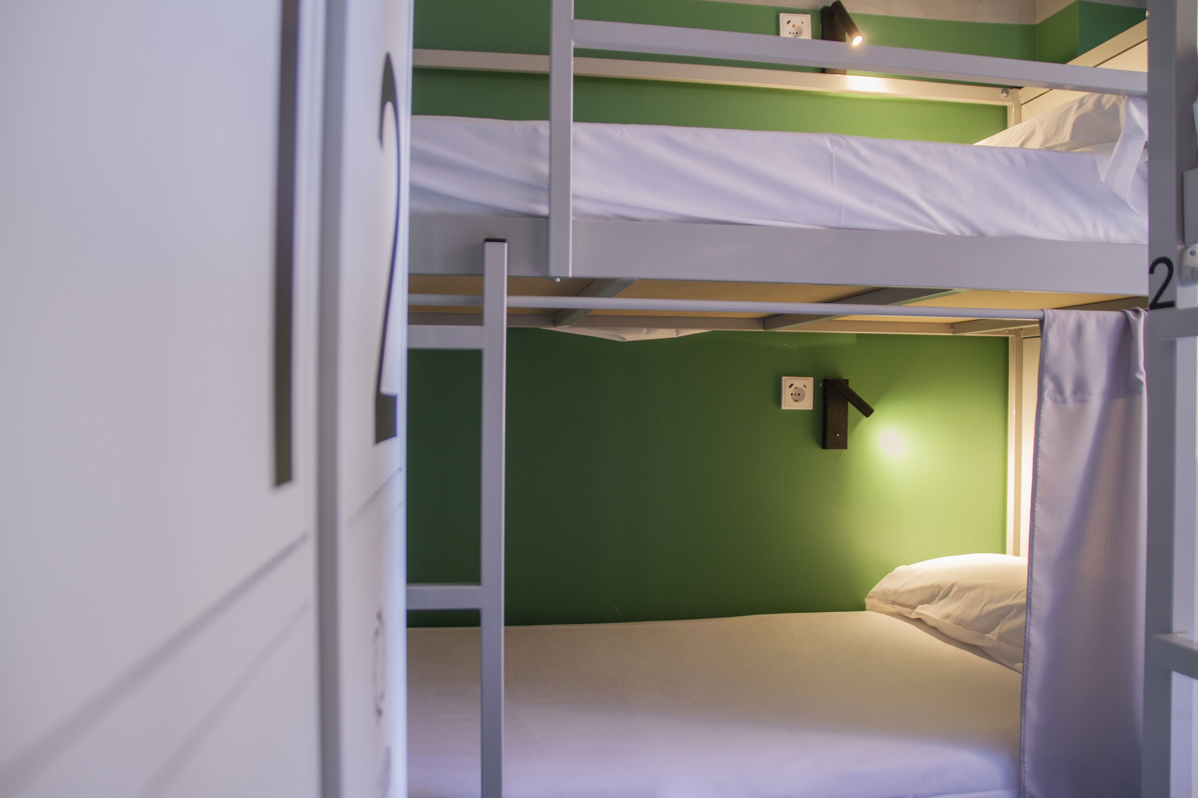 Une chambre avec un lit superposé, aux murs verts et au linge de lit blanc.