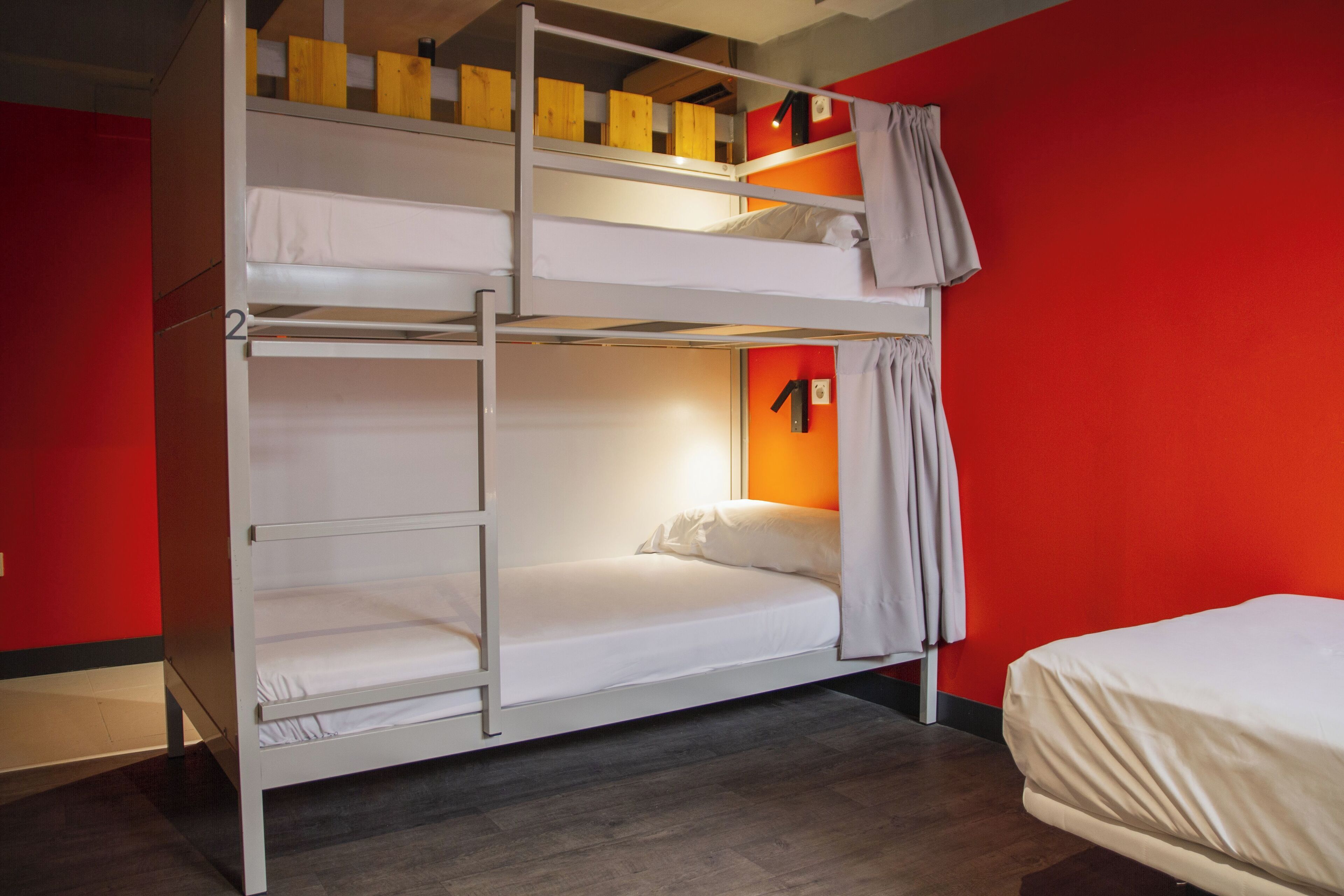 Dormitorio con literas, pared roja, cabecera de madera y una ventana pequeña con cortinas.