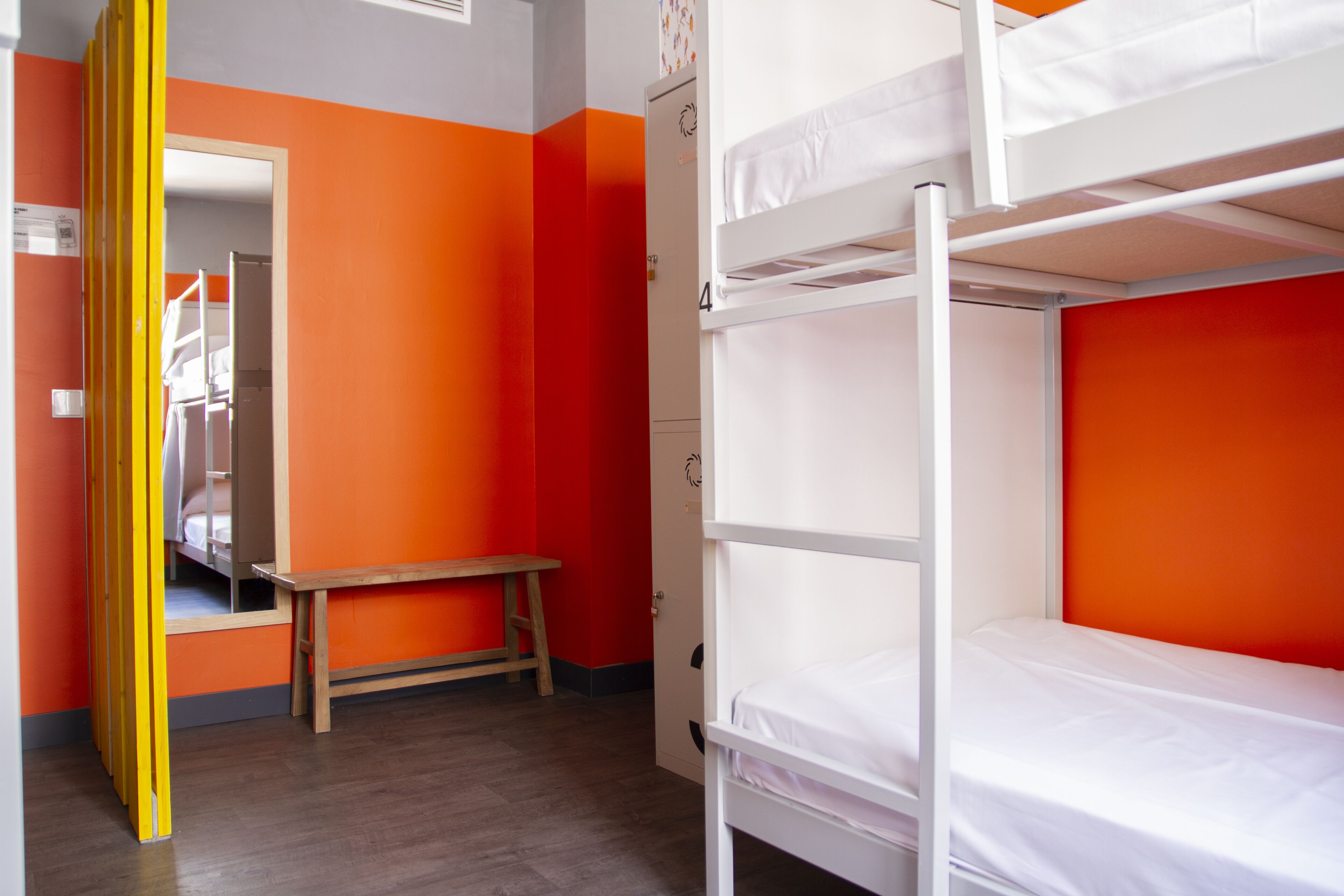 A bunk bed room with orange walls, a wooden bench, and a door leading to another room.