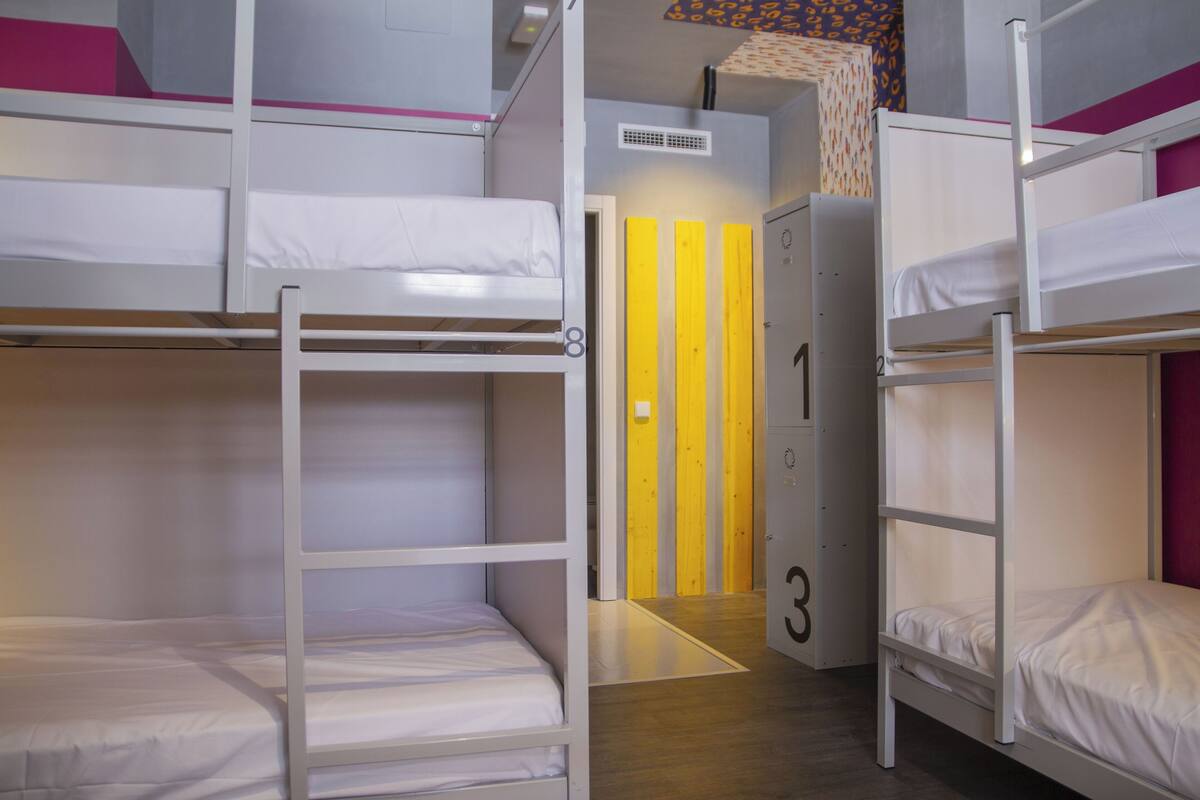 Um quarto tipo dormitório com beliches, uma porta com número e uma cortina estampada.