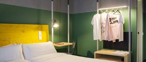 Una habitación de hotel con una cama, un escritorio y un perchero con camisetas.