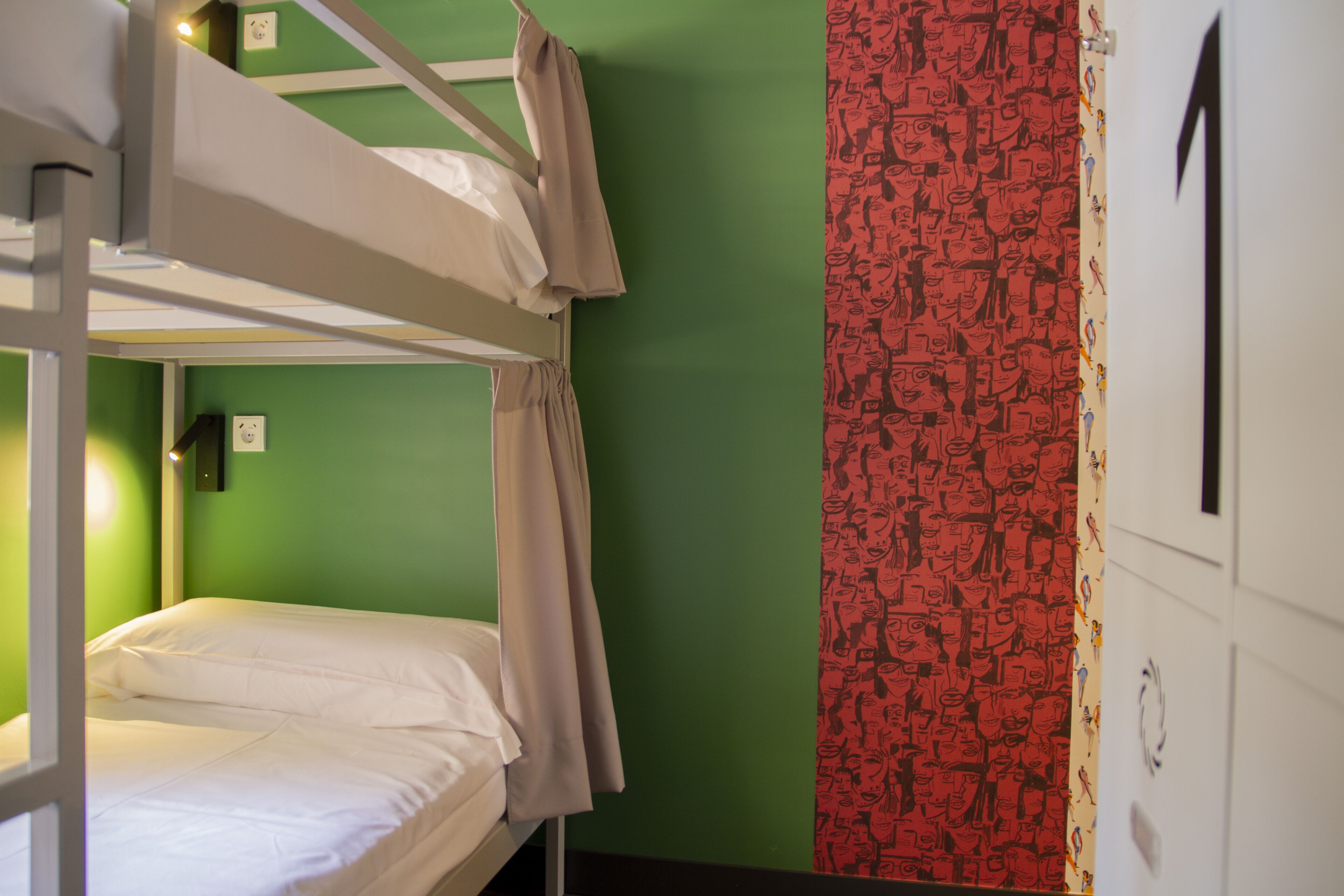 A bunk bed room with green walls, a red patterned curtain, and a white door with a number.