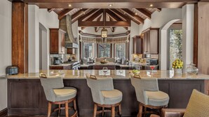 A spacious kitchen with a large island, wooden bar stools, and a view through the windows. - Luxury Ski-in/out Estate Hot tub + Game Room Paragon (Avon)