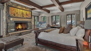 A bedroom with a stone fireplace, a large bed, and a television. - Luxury Ski-in/out Estate + Game Room | Paragon (Avon)