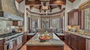 A spacious kitchen with a central island, wooden cabinets, and a large window providing a view of trees. - Luxury Ski-in/out Estate Hot tub + Game Room Paragon (Avon)