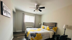 Ein Schlafzimmer mit einem Bett, einem Deckenventilator, einem Nachttisch und einem Fenster mit Vorhängen.