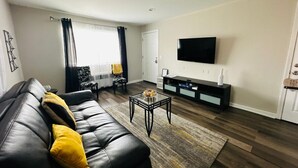 Ein Wohnzimmer mit einem schwarzen Ledersofa, einem Glastisch und einem an der Wand montierten Flachbildfernseher.
