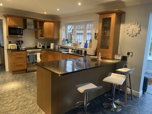 A modern kitchen with wooden cabinets, a large island with bar stools, a built-in oven, and a microwave.