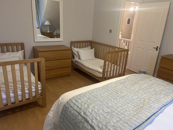 A bedroom with a large bed, two wooden cribs, a dresser, and a mirror.