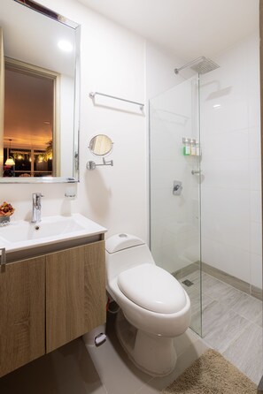 A modern bathroom with a glass-enclosed shower, a white toilet, a wooden vanity, and a large mirror. - Moderno Apartamento con diseño caribe (Cartagena)