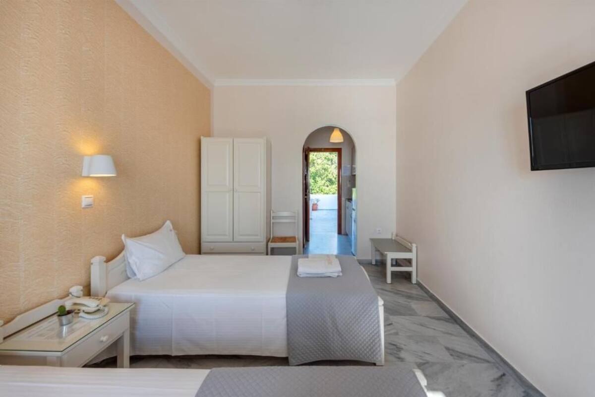 Habitación de hotel con cama, mesita de noche, lámpara, armario y televisor montado en la pared.