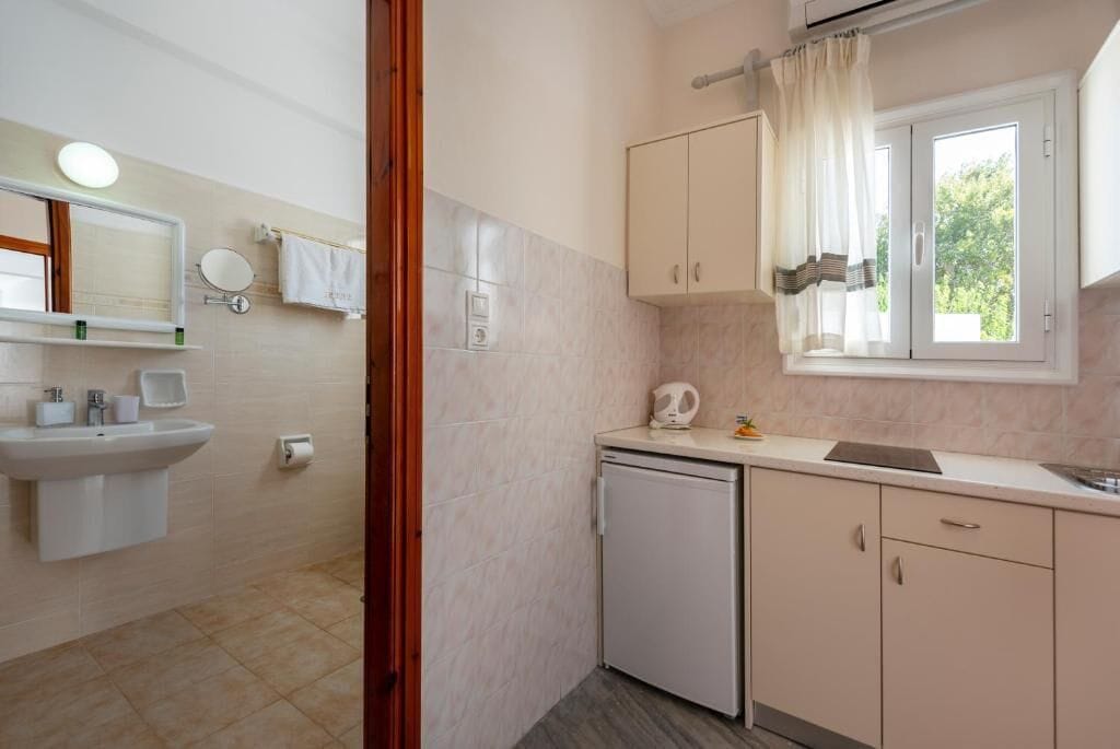 A compact kitchen with a sink, a small refrigerator, and a window with curtains.